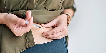 Eine Frau setzt sich selber eine Spritze in den Bauch.