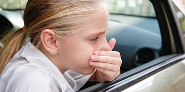 Reisekrankheit Ein Mädchen schaut aus dem offenen Autofenster und hält sich die Hand vor den Mund.