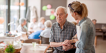 Foto: Eine Pflegekraft st&uuml;tzt einen &auml;lteren Herren