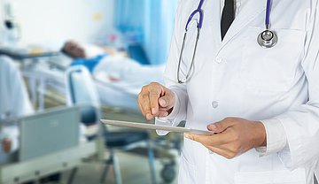 Ein Arzt in Nahaufnahme steht in einem Krankenzimmer und tippt auf sein Tablet.