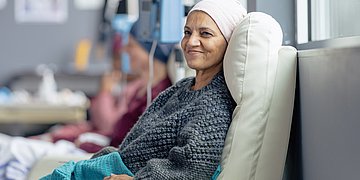 Foto: Eine Frau mittleren Alters mit Kopfbedeckung liegt auf einer Liege und bekommt eine Chemoinfusion.