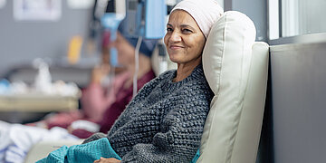 Foto: Eine Frau mittleren Alters mit Kopfbedeckung liegt auf einer Liege und bekommt eine Chemoinfusion.