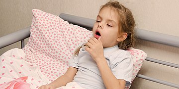 Keuchhusten Foto: Ein kleines Mädchen liegt im Bett und hustet.