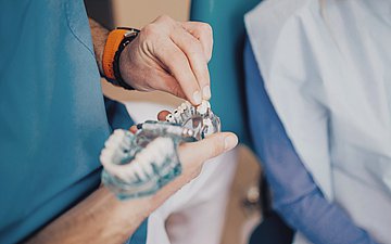 Zahnersatz Foto von einer Hand, die ein provisorisches Gebiss mit einem separaten Zahn in der Hand hält.