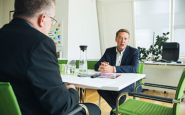 An einem Schreibtisch sitzen G+G Autor Thorsten Severin (von hinten), der mit Herrn Hildenbrand (von vorne) das Interview f&uuml;hrt.