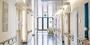 Ein leerer Krankenhausflur. Am Ende steht ein Bett rechts an der Wand.