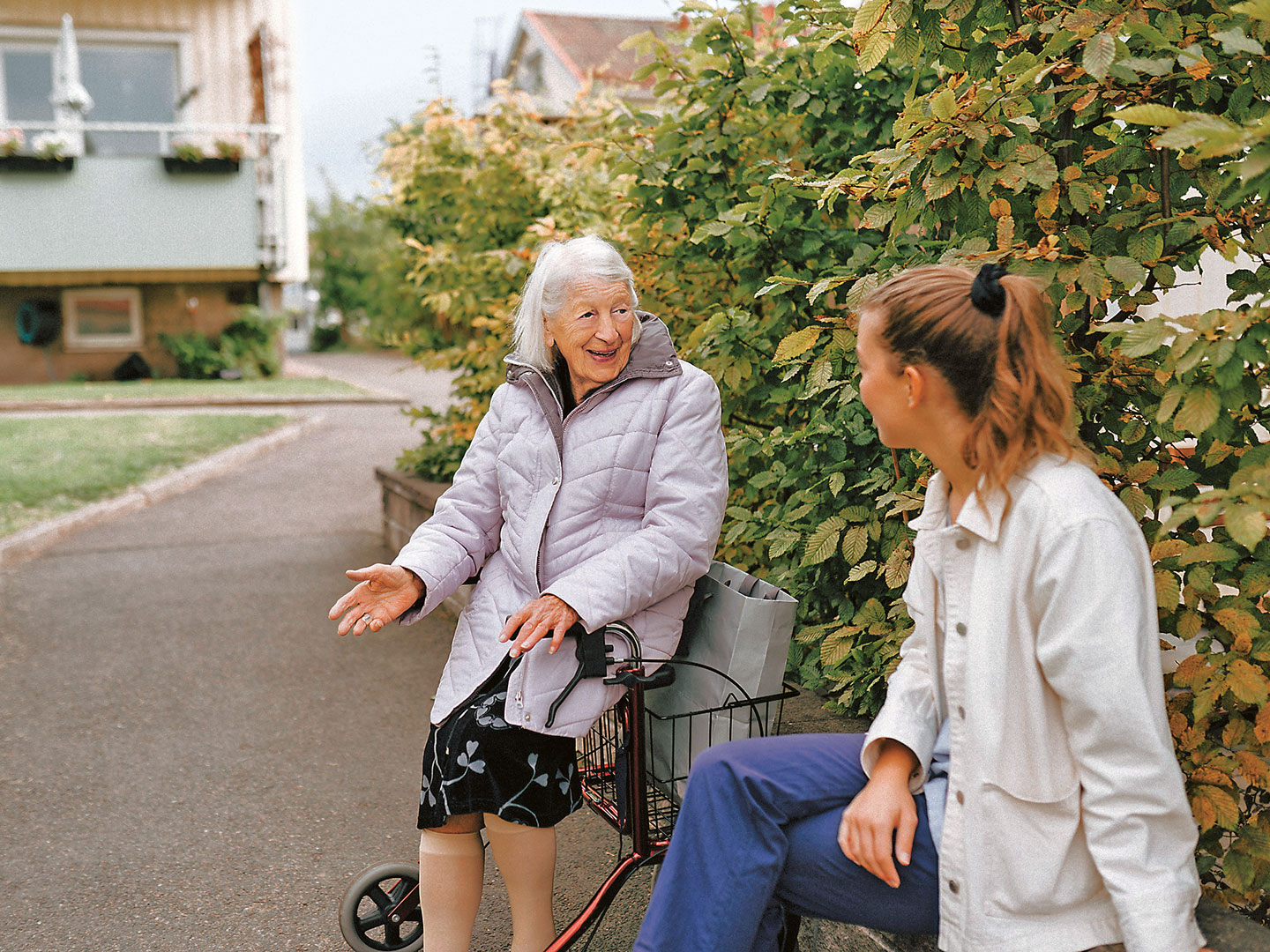 Foto einer alten Dame mit Rollator, die im Freien mit einer jungen Frau spricht