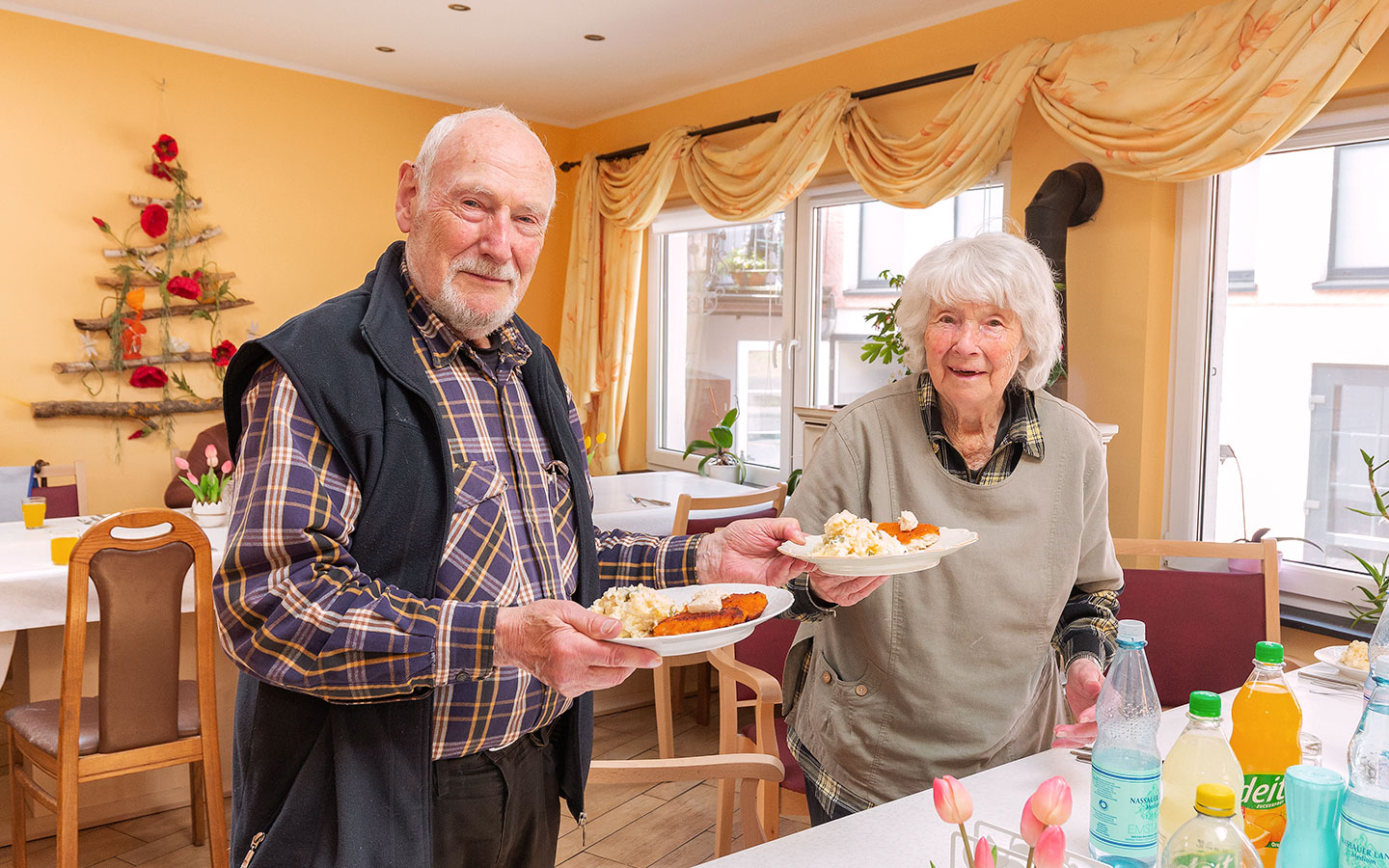 Foto: Ein Ehepaar, das auf einem Pflegebauernhof lebt, hält jeweils einen Teller mit Essen in der Hand.
