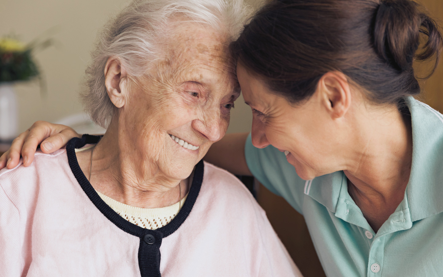 Foto: Eine pflegende Frau umarmt eine ältere Frau und lächelt.