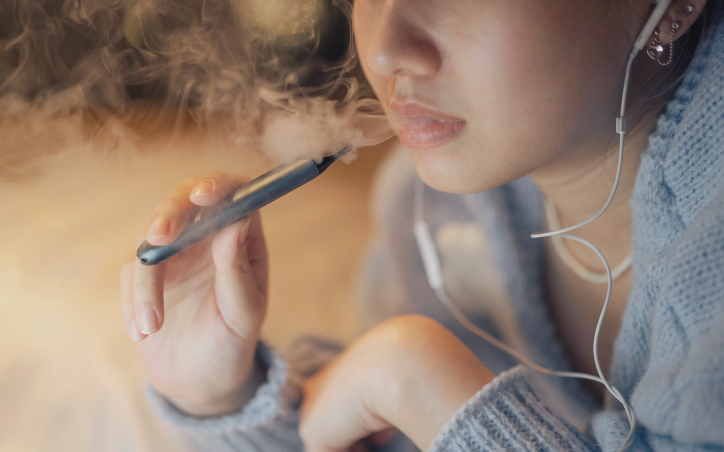 Foto: Eine Frau hält eine E-Zigarette in der Hand und bläst Rauch aus.