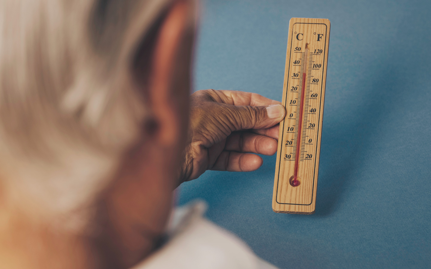 Foto: Eine ältere Person hält ein Thermometer in der Hand, das circa 35 Grad anzeigt.