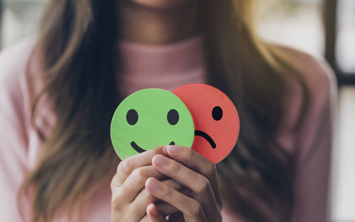 Foto: Eine Frau hält in ihren Händen zwei Symbole – eines zeigt einen lachenden, das andere einen weinenden Smiley.