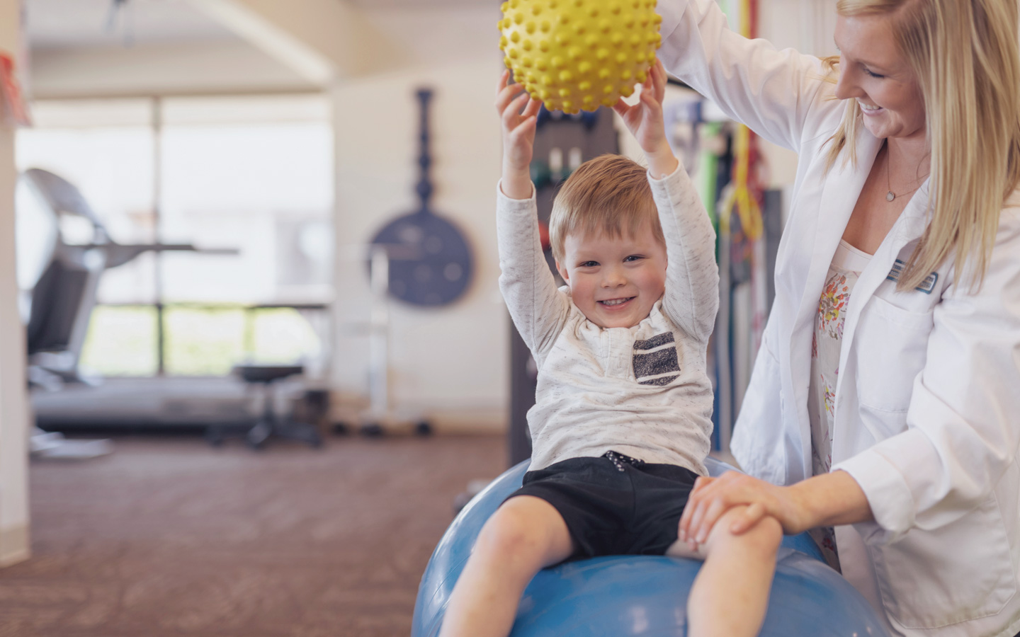 Eine Physiotherapeutin macht mit einem Kind Übungen mit einem Ball.