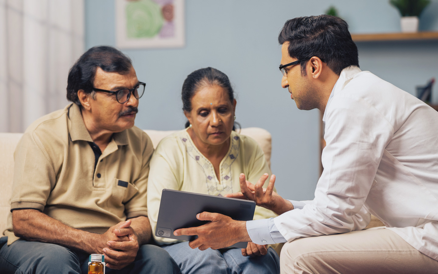 Eine Arzt zeigt einer Frau und einem Mann auf einem Tablet medizinische Angaben.