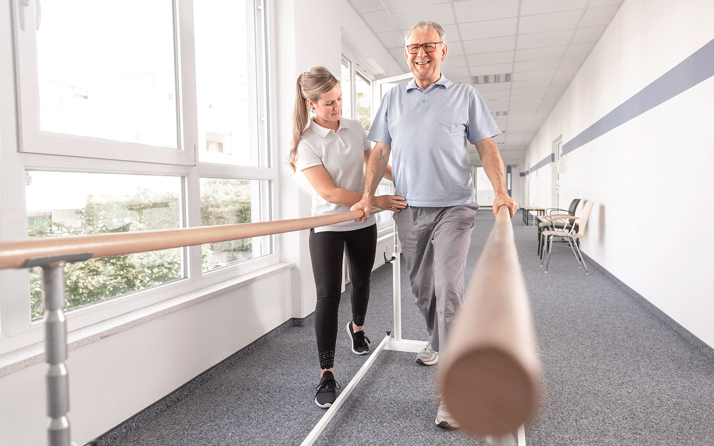 Foto: Ein Mann trainiert mit Unterstützung einer Physiotherapeutin Gehen an Hilfsstangen.