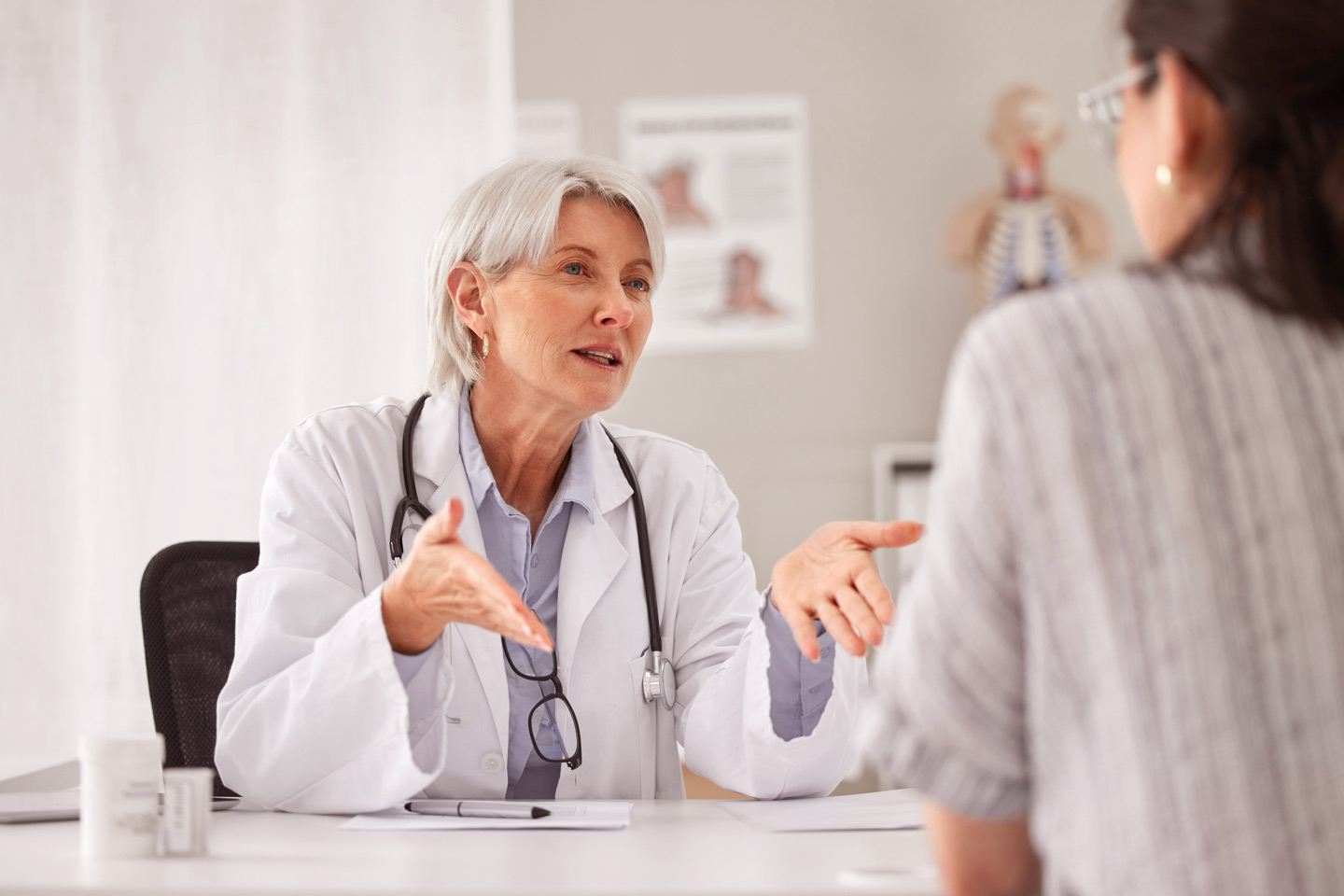 Foto: Eine Ärztin spricht mit einer Patientin. Beide sitzen sich an einem Schreibtisch gegenüber.