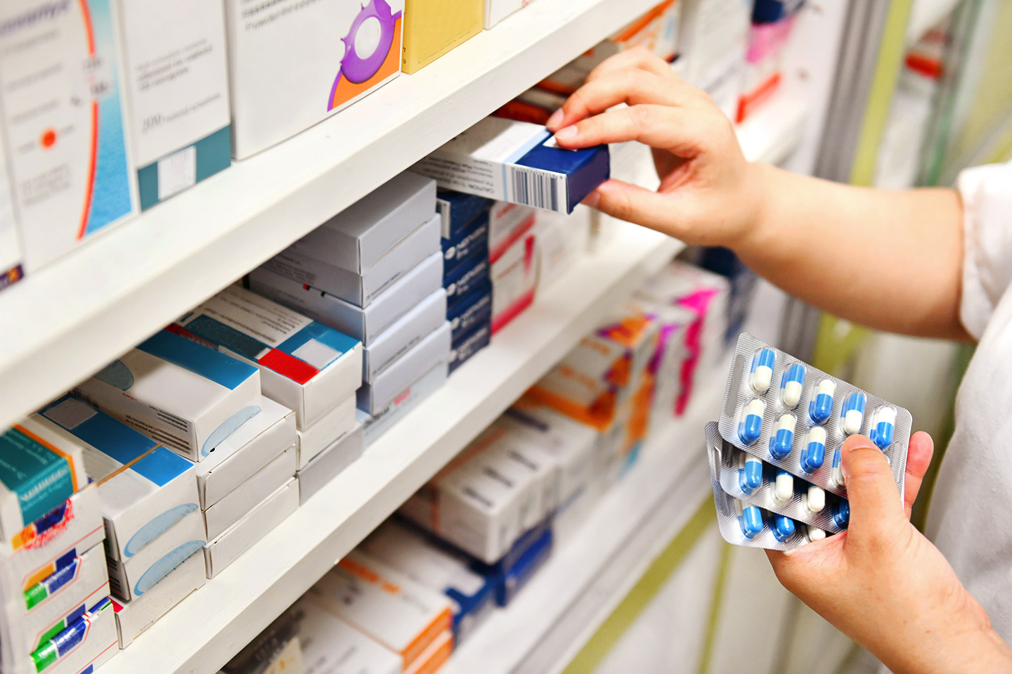 Foto: Zwei Hände sortieren Medikamente in einem Arzneimittel-Regal.