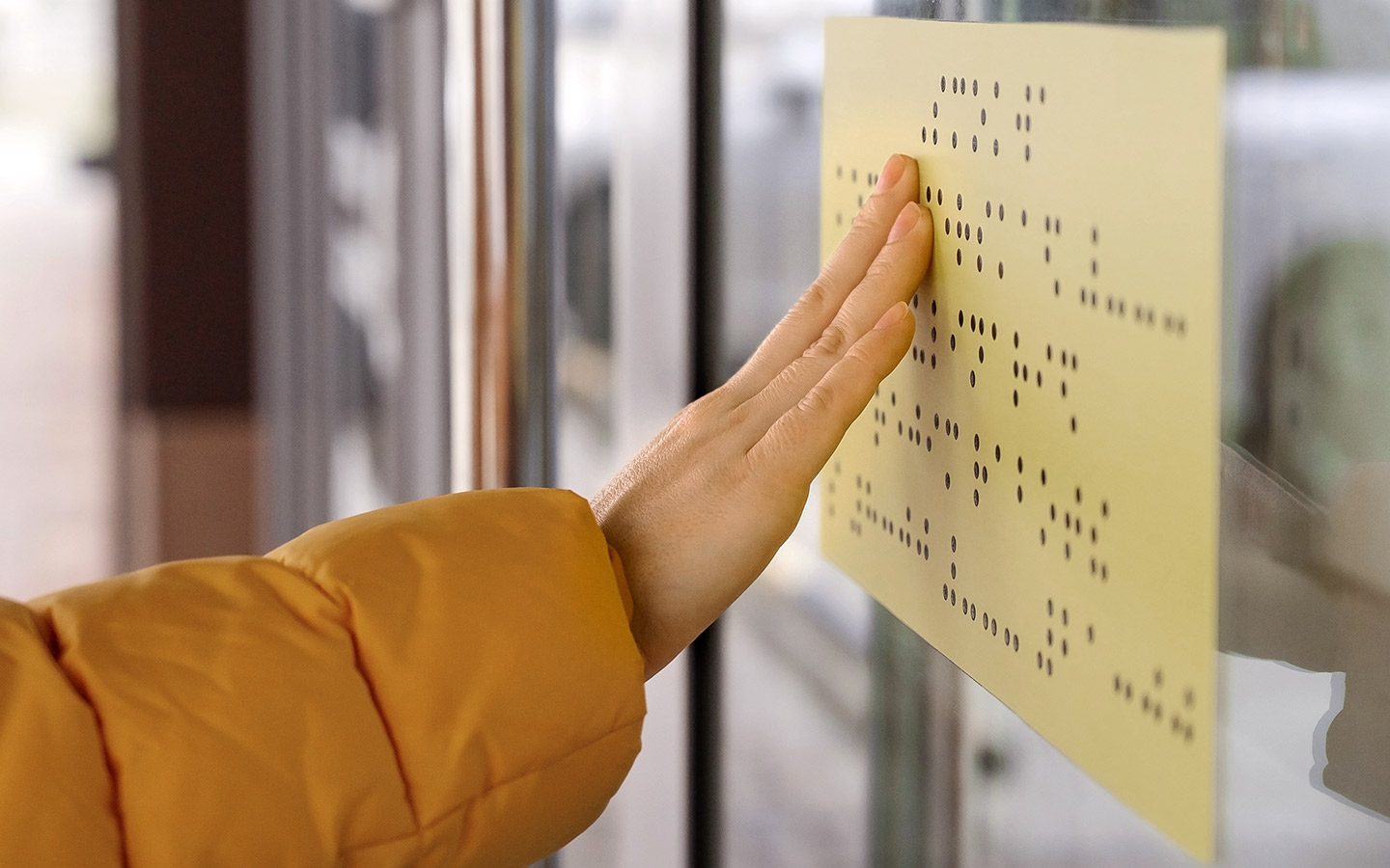 Foto: Eine Hand tastet einen Informationsaushang mit Brailleschrift ab.