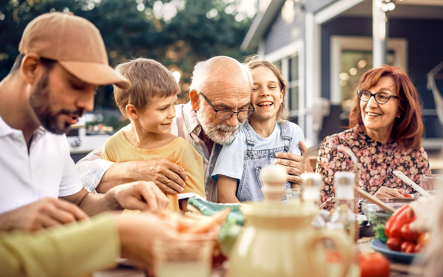 Foto: Familie aus drei Generationen sitzt im Garten am Tisch beim Essen.