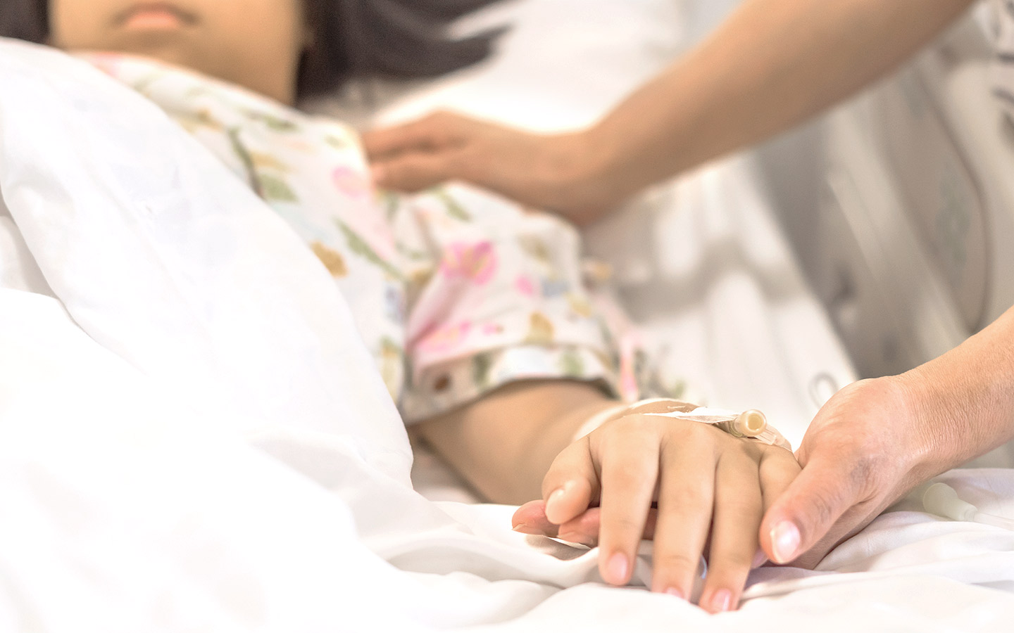 Foto: todkrankes Mädchen liegt im Krankenhausbett, Erwachsene hält ihre Hand.