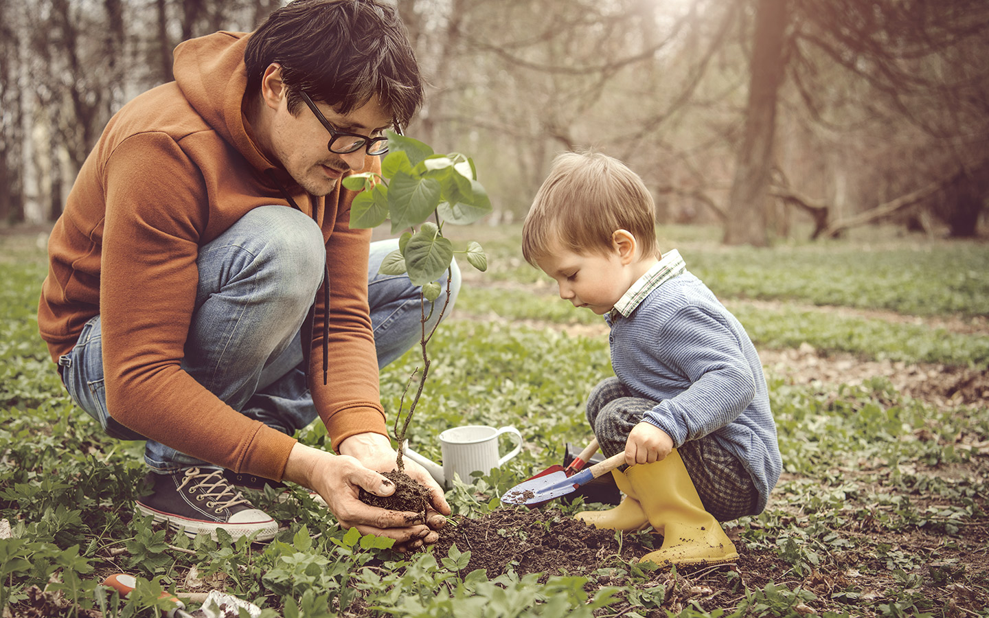 Foto: Ein Kind und ein Mann pflanzen ein kleines Bäumchen ein.