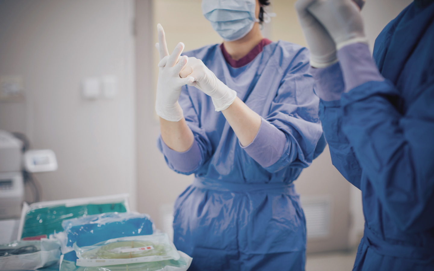Foto: Krankenhauspersonal trägt Mundschutz, OP-Kleidung und sie ziehen sich Handschuhe an
