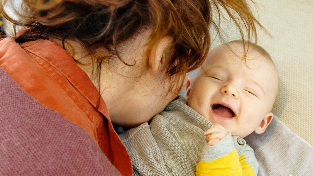 Eine Frau pustet einem lachenden Baby auf die Brust.
